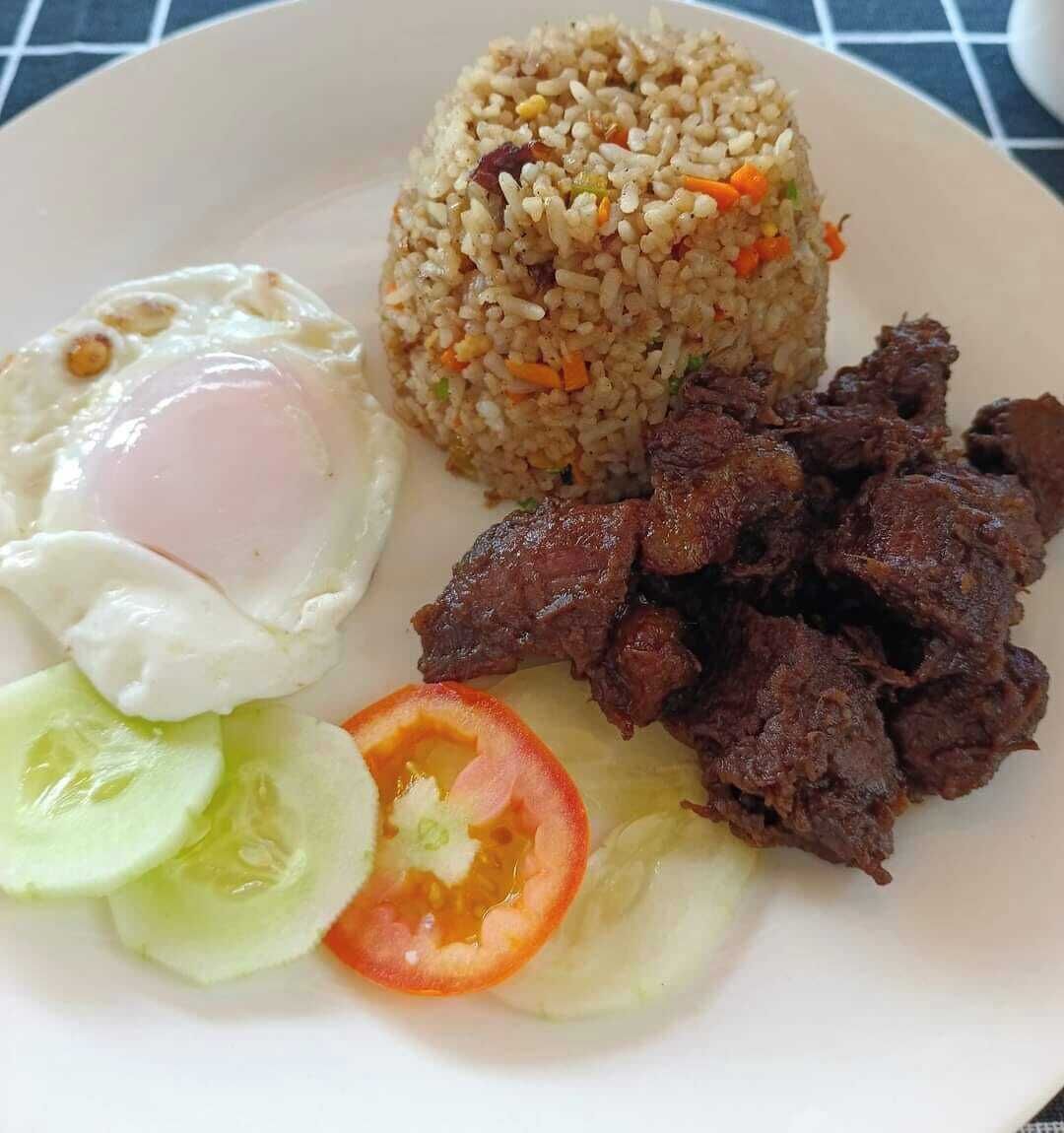 A plate of fried rice with vegetables, a fried egg, and slices of meat.