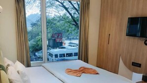 A modern hotel room with a large bed, a TV mounted on the wall, and a view of a bus outside the window. - Rajasthani Hotel Dhani (Sonapur)