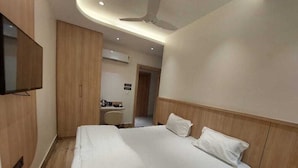 A modern hotel room with a large bed, a flat-screen TV mounted on the wall, and a ceiling fan. - Rajasthani Hotel Dhani (Sonapur)