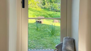 A door with a view of a garden, a black handle, and a woven basket with a patterned pillow. - Hop at Tipsy Cottages: a romantic rural retreat (Robertsbridge)