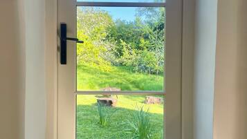 A door with a view of a garden, a black handle, and a woven basket with a patterned pillow.