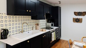 A kitchen with black cabinets, a white countertop, a microwave, and a coffee maker. - Hop at Tipsy Cottages: a romantic rural retreat (Robertsbridge)
