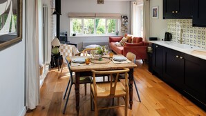 A dining area with a wooden table set for two, a red sofa, and a kitchen with black cabinets. - Hop at Tipsy Cottages: a romantic rural retreat (Robertsbridge)