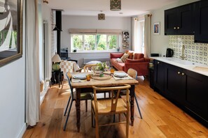 A dining area with a wooden table set for two, a red sofa, and a kitchen with black cabinets.