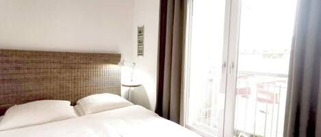 A hotel room with a bed, a nightstand, a lamp, and a view through a sliding glass door.