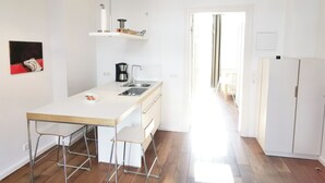 A modern kitchen with a white countertop, stainless steel sink, and a coffee maker. There are bar stools and a hanging light fixture. - Ferienwohnung Schuppen XII mit Terrasse (Norderney)