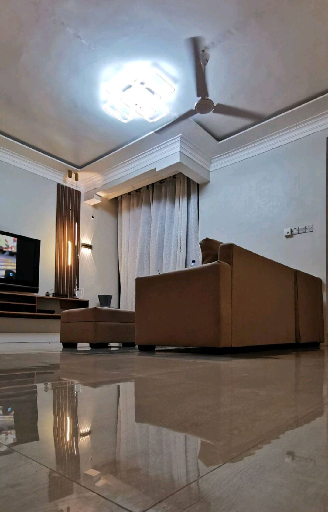 Ein modernes Wohnzimmer mit einer großen Couch, einem Deckenventilator und einem Flachbildfernseher.