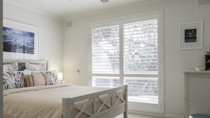 Ein Schlafzimmer mit einem Bett, einem Fenster mit Jalousien, einem an der Wand befestigten Regal und einem gerahmten Bild.