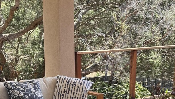 Eine Holzterrasse mit einer Couch und Hocker, umgeben von viel Grün.