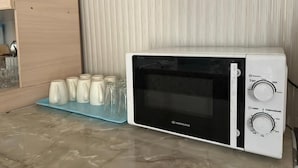 A white microwave oven with a digital display and control knobs, placed on a blue tray with several glass containers. - Sunny Hostel (Osh)