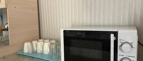 A white microwave oven with a digital display and control knobs, placed on a blue tray with several glass containers.