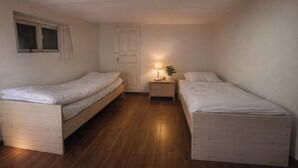 A small, single-room accommodation with two wooden beds, a nightstand with a lamp, and a window with curtains. - Sunny Hostel (Osh)