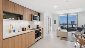 A modern kitchen with a built-in microwave, oven, and sink. There is a dining area with a sofa and chairs. - High-Rise Balcony: Ocean Views, Pool & Spa (Miami)