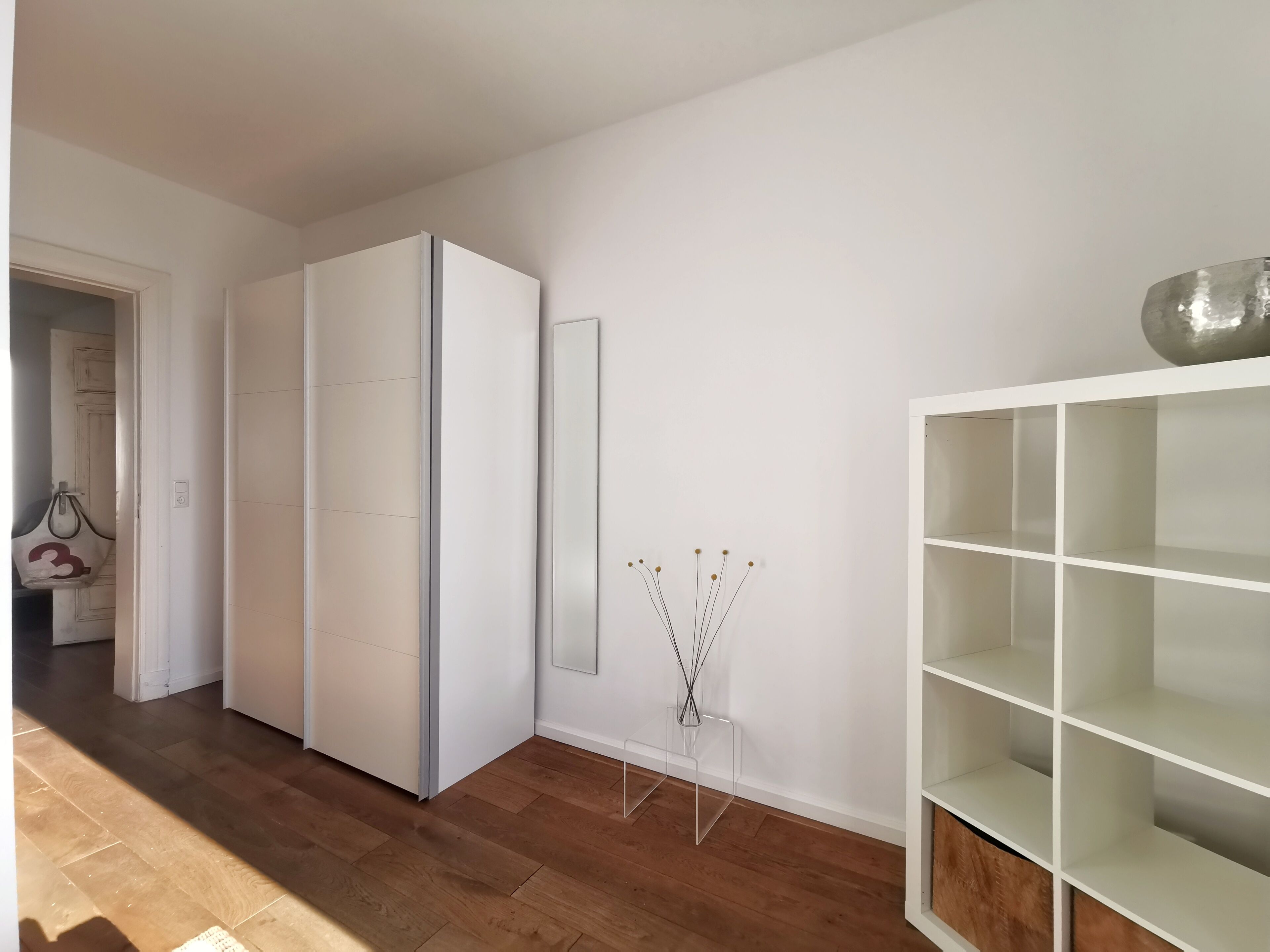 A modern room with a white wardrobe, a mirror, and a white shelving unit.