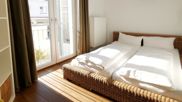 A hotel room with a large bed, a wicker bench, a view through a sliding door, and a wall-mounted sculpture. - Vacation apartment Schuppen XIII with spacious terrace  (Norderney)