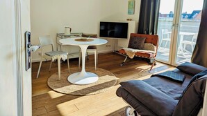 Uma sala de estar com uma mesa redonda branca, um sofá marrom e uma televisão.