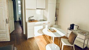 Uma cozinha compacta com armários brancos, uma pia pequena e uma mesa redonda com cadeiras.