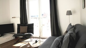 Uma sala de estar moderna com um sofá, uma poltrona, uma mesa de centro, uma televisão e um abajur.