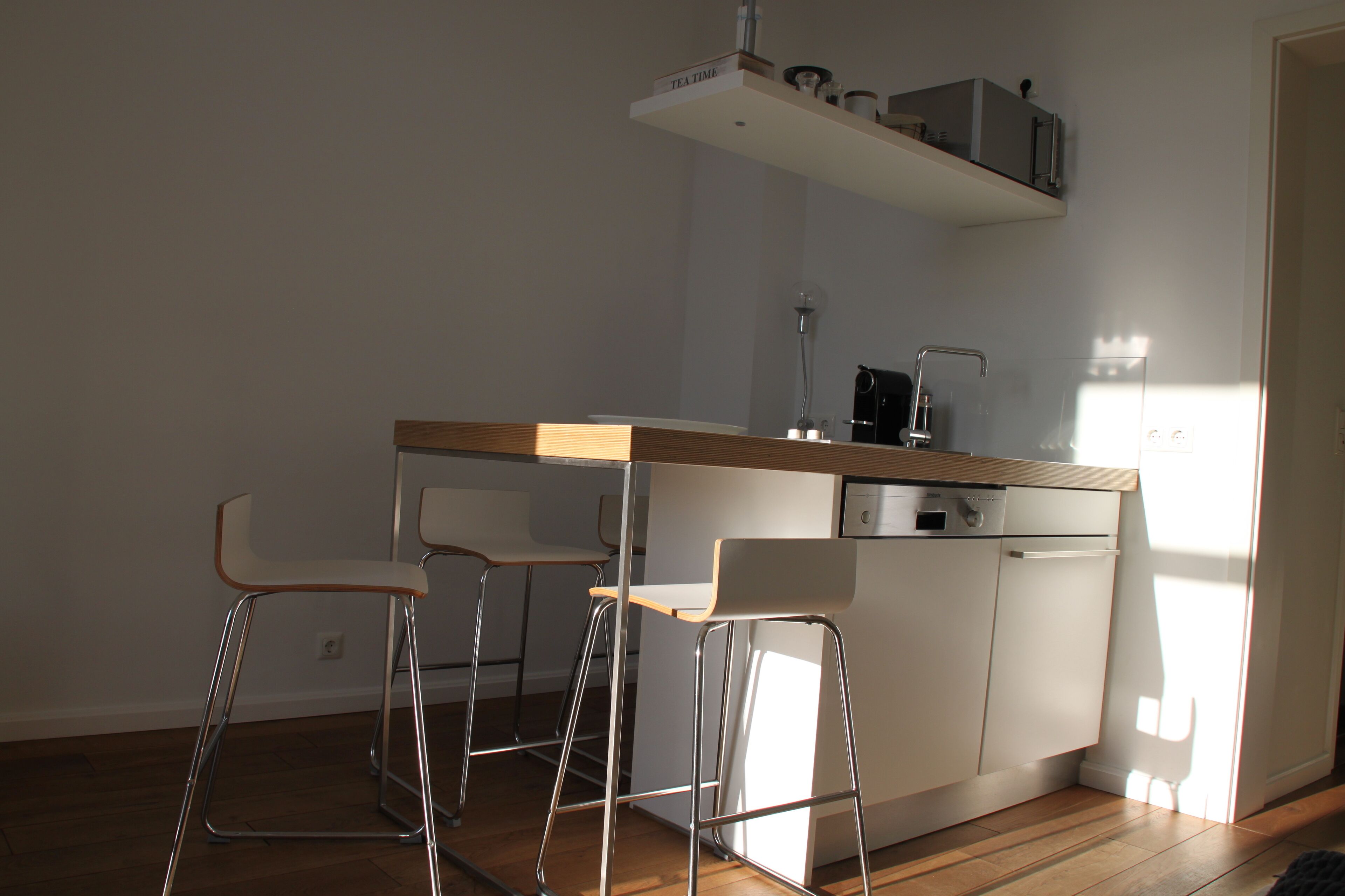 A modern kitchen with a wooden countertop, two bar stools, a dishwasher, and a coffee machine.