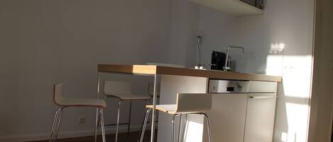 A modern kitchen with a wooden countertop, two bar stools, a dishwasher, and a coffee machine.