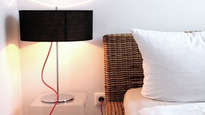 Een moderne kamer met een opgeruimd nachtkastje, een lamp met een rode kabel, een wit kussen en een rieten hoofdbord.