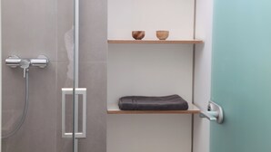 Een badkamer met een douchecabine van glas, een handdoekrek en twee houten planken met kommen en een opgevouwen handdoek.