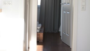 Un pasillo con una puerta que da a una habitación, una cesta en el suelo y una ventana con cortinas.