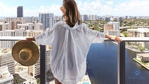 A person standing on a balcony with a cityscape view, holding a straw hat. - 3 BR Apartment with amazing View,  Pool and  Gym (Hollywood)