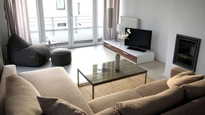 A modern living room with a sofa, a glass coffee table, a flat-screen TV, and a fireplace. - Apartment Schuppen III with balcony and terrace (Rerik)