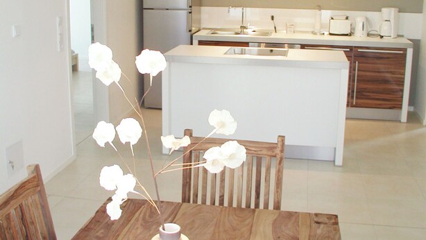 A modern kitchen with a central island, a dining table with chairs, and a vase with white flowers. - Apartment Schuppen III with balcony and terrace (Rerik)
