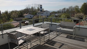 A rooftop terrace with outdoor furniture, a view of the surrounding neighborhood, and a lighthouse in the distance. - Shed VI - Penthouse with sea view  (Rerik)