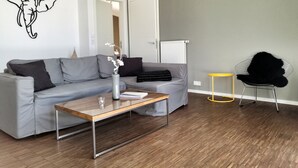 A modern living room with a grey sectional sofa, a wooden coffee table, a black chair, and a yellow side table. - Shed VI - Penthouse with sea view  (Rerik)