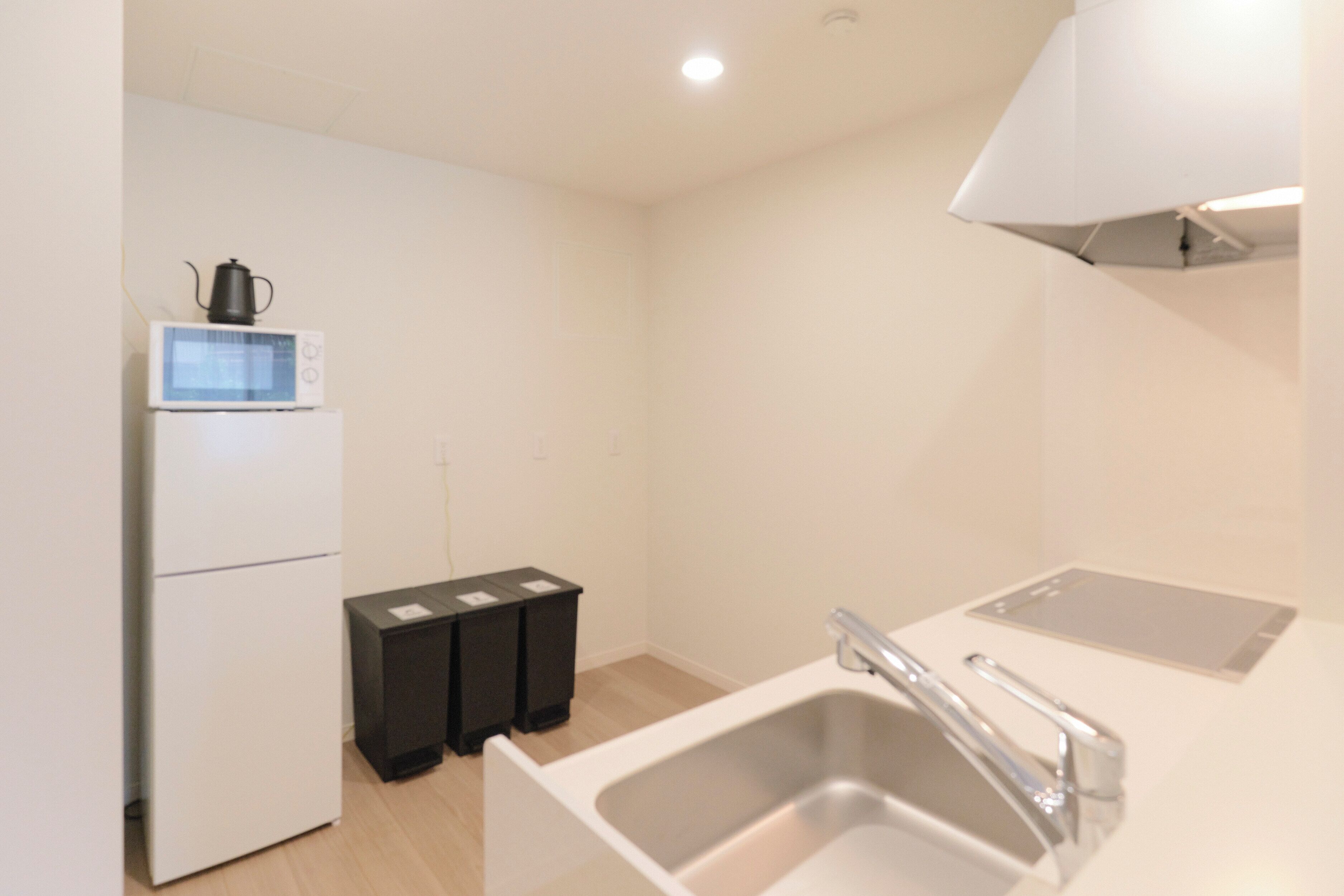 A small kitchenette with a microwave, refrigerator, sink, and black trash bins.