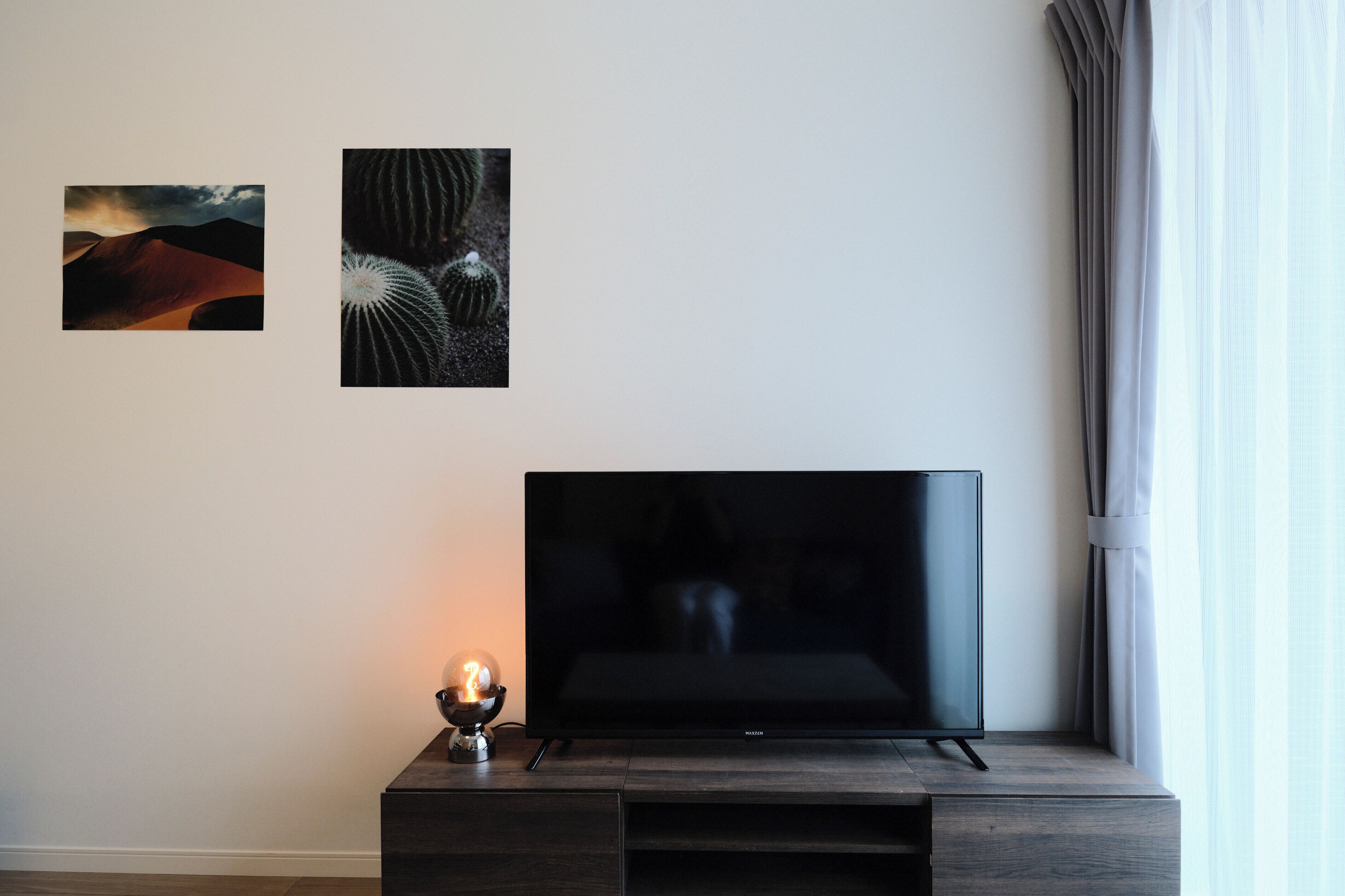 A modern living room with a flat-screen TV on a wooden stand, two framed abstract artworks on the wall, and a table lamp with a spherical base.