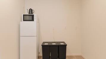 Una kitchenette con un refrigerador blanco, un microondas y una tetera encima. Hay tres botes de basura negros pegados a la pared.