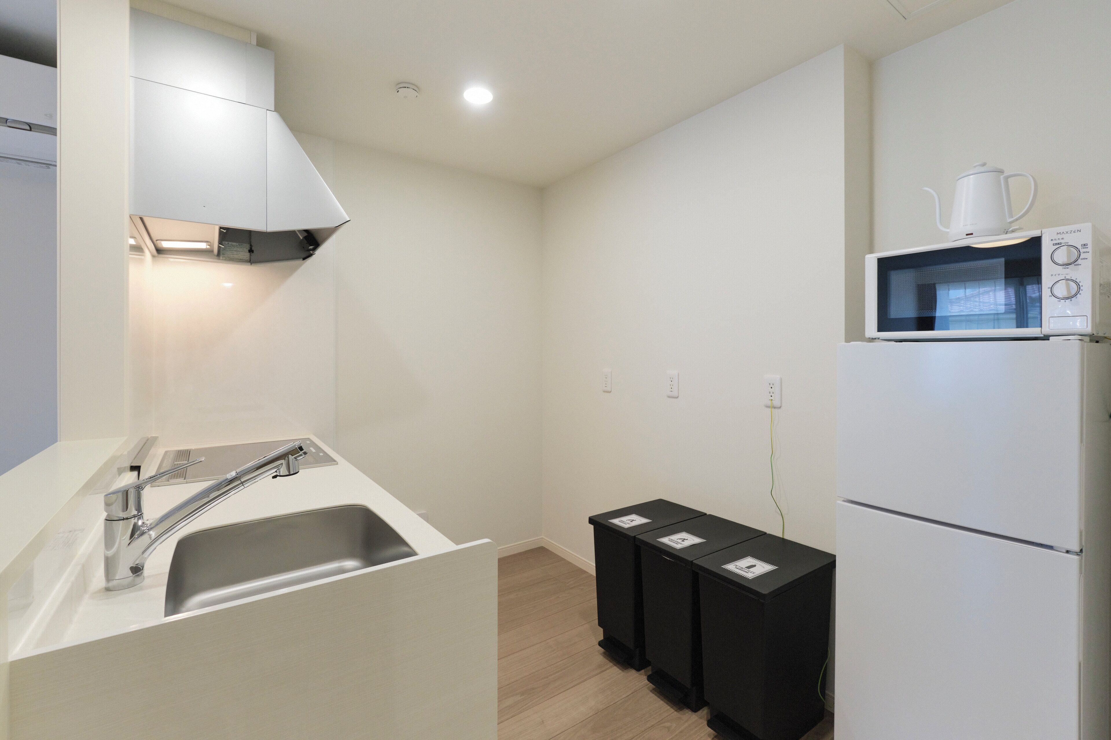 Una cocina moderna con un lavamanos de acero inoxidable, armarios blancos, un microondas y botes de basura negros.