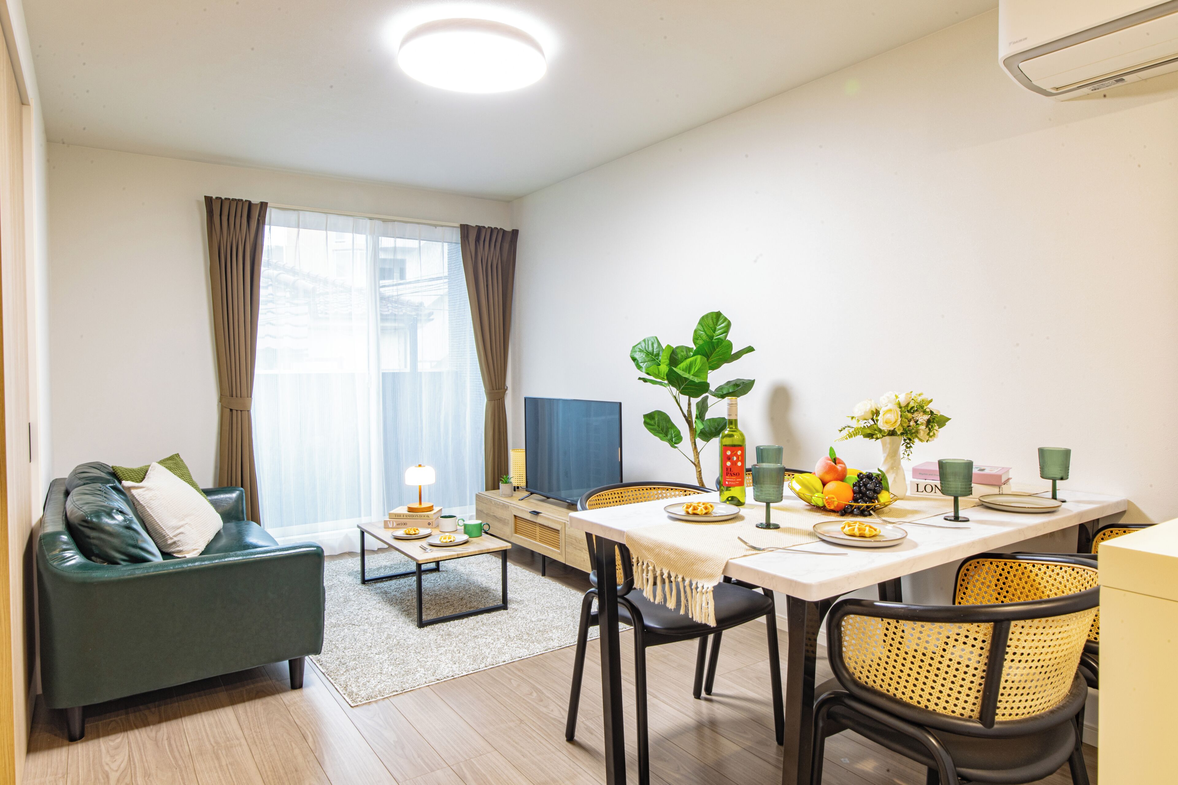 Een moderne woonkamer met een bank, een eettafel met stoelen, een televisie en een plant.