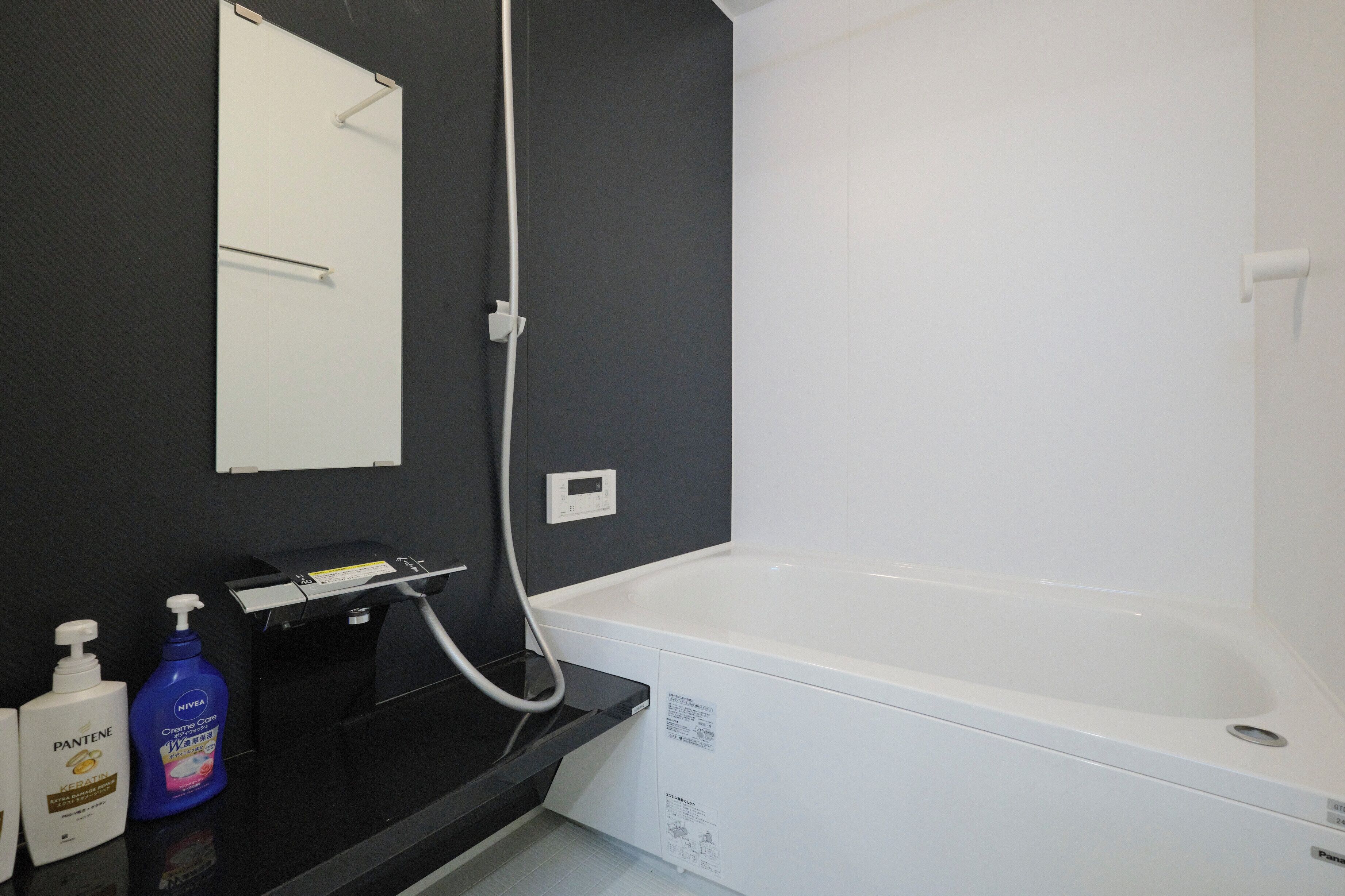 A bathroom with a white bathtub, a black countertop, and a mirror. There are two bottles of hand soap on the counter.