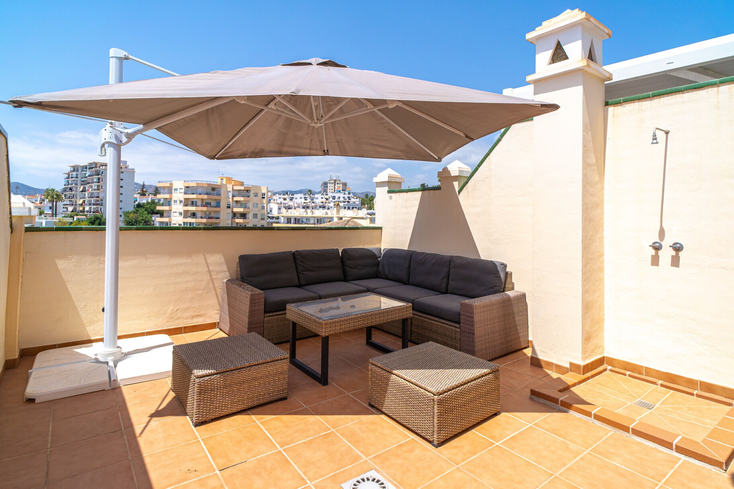 Une terrasse sur le toit aménagée avec un canapé d’angle, deux petites tables d’appoint et un grand parasol pour créer de l’ombre.