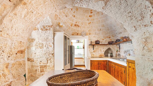 A rustic kitchen with stone walls, wooden cabinets, and a woven basket on the table. - 3834 Villa La Bianca Ostuni by Barbarhouse (Carovigno)