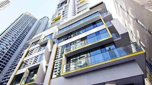A modern high-rise building with multiple floors, large windows, and a prominent yellow accent on the facade.