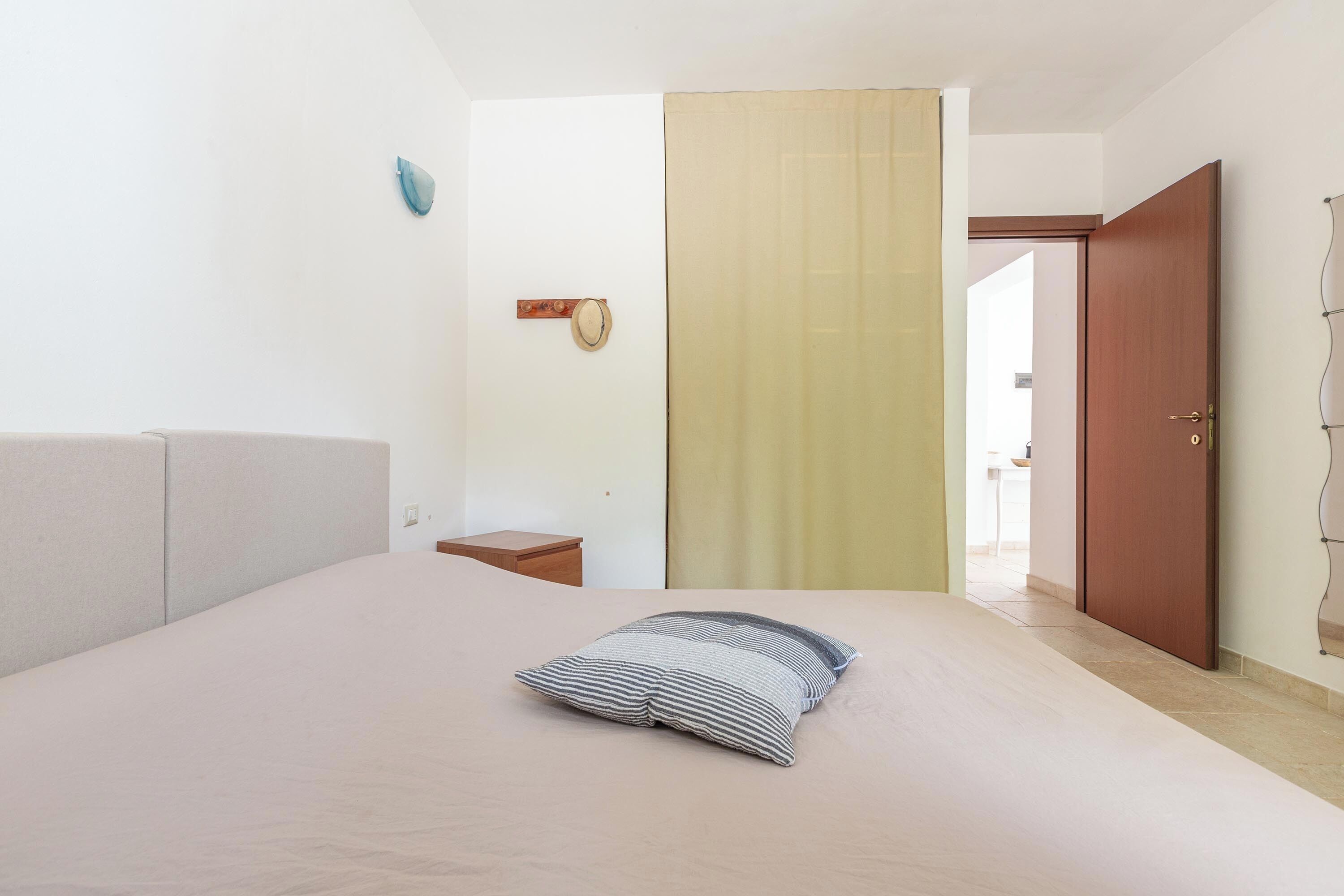 Ein Schlafzimmer mit einem Bett, einem Nachttisch, einer Wanduhr und einer Tür zu einem anderen Raum.
