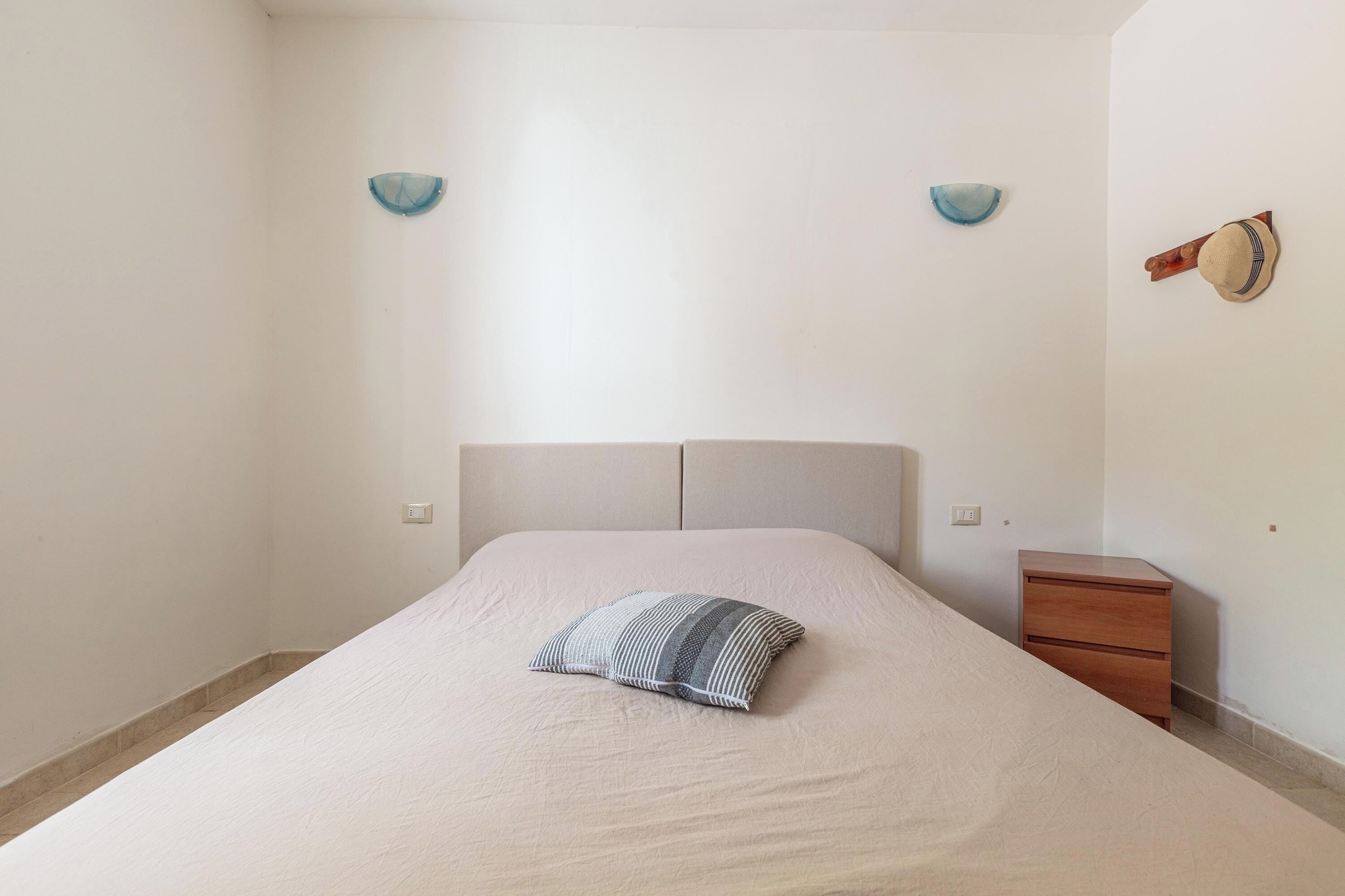 Un dormitorio con una cama, una mesita de noche y dos lámparas fijadas a la pared.