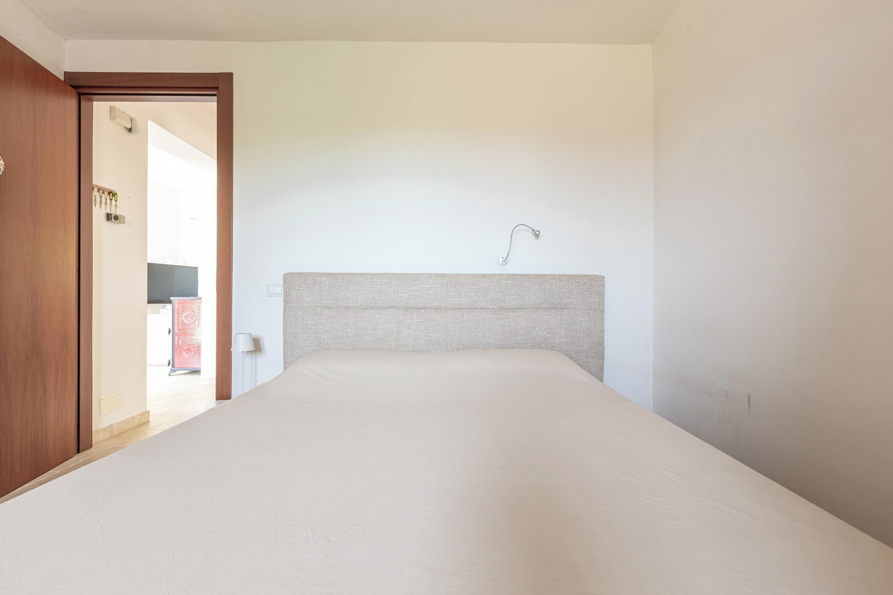 A bedroom with a large bed, a wooden door, and a view into another room with a red cabinet.
