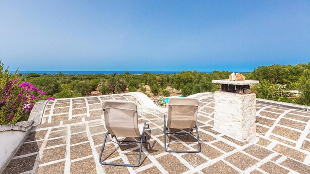 Two chairs on a tiled patio overlooking a scenic view of the sea and greenery. - 4099 Villa Maste by Barbarhouse (Carovigno)