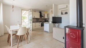 A modern kitchen with white cabinets, a dining area with a white table and chairs, and a red wood-burning stove. - 4099 Villa Maste by Barbarhouse (Carovigno)