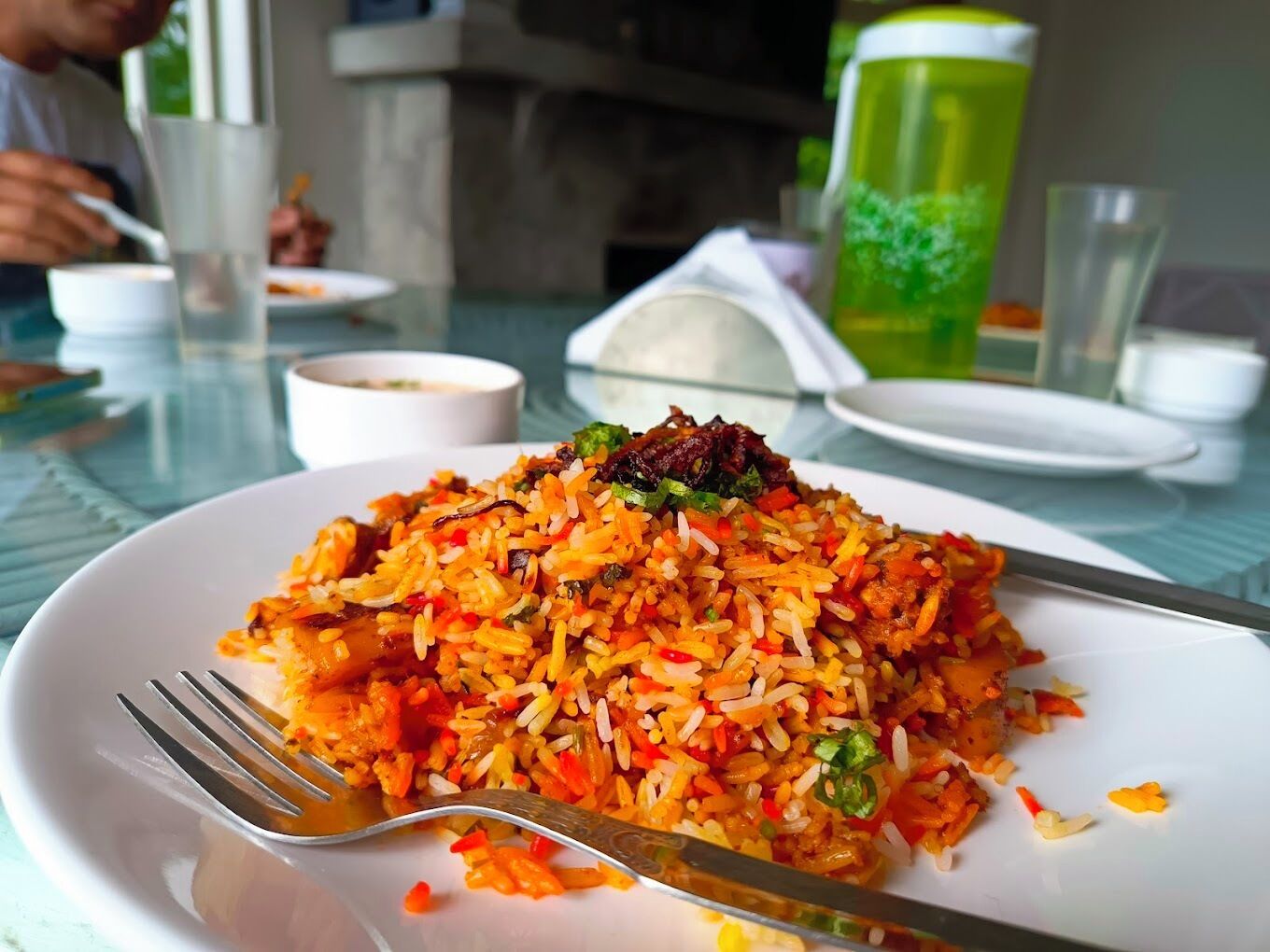 A plate of fried rice with vegetables and meat, served on a white plate with a fork and knife.