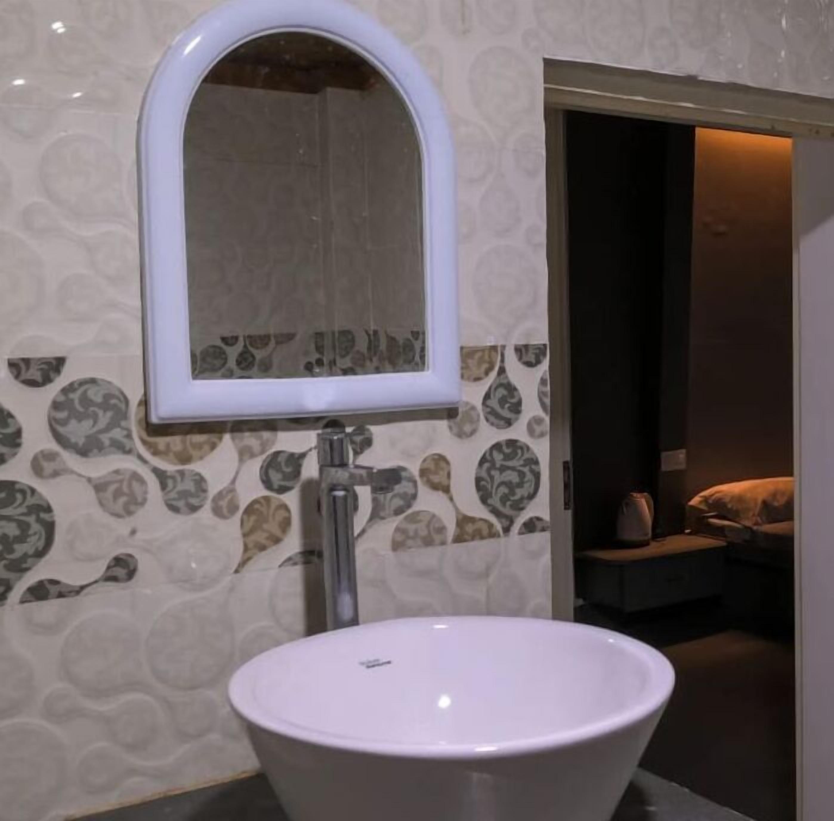 Ein Badezimmer mit einem weißen Waschbecken, einem Spiegel und wandfarbiger Tapete.