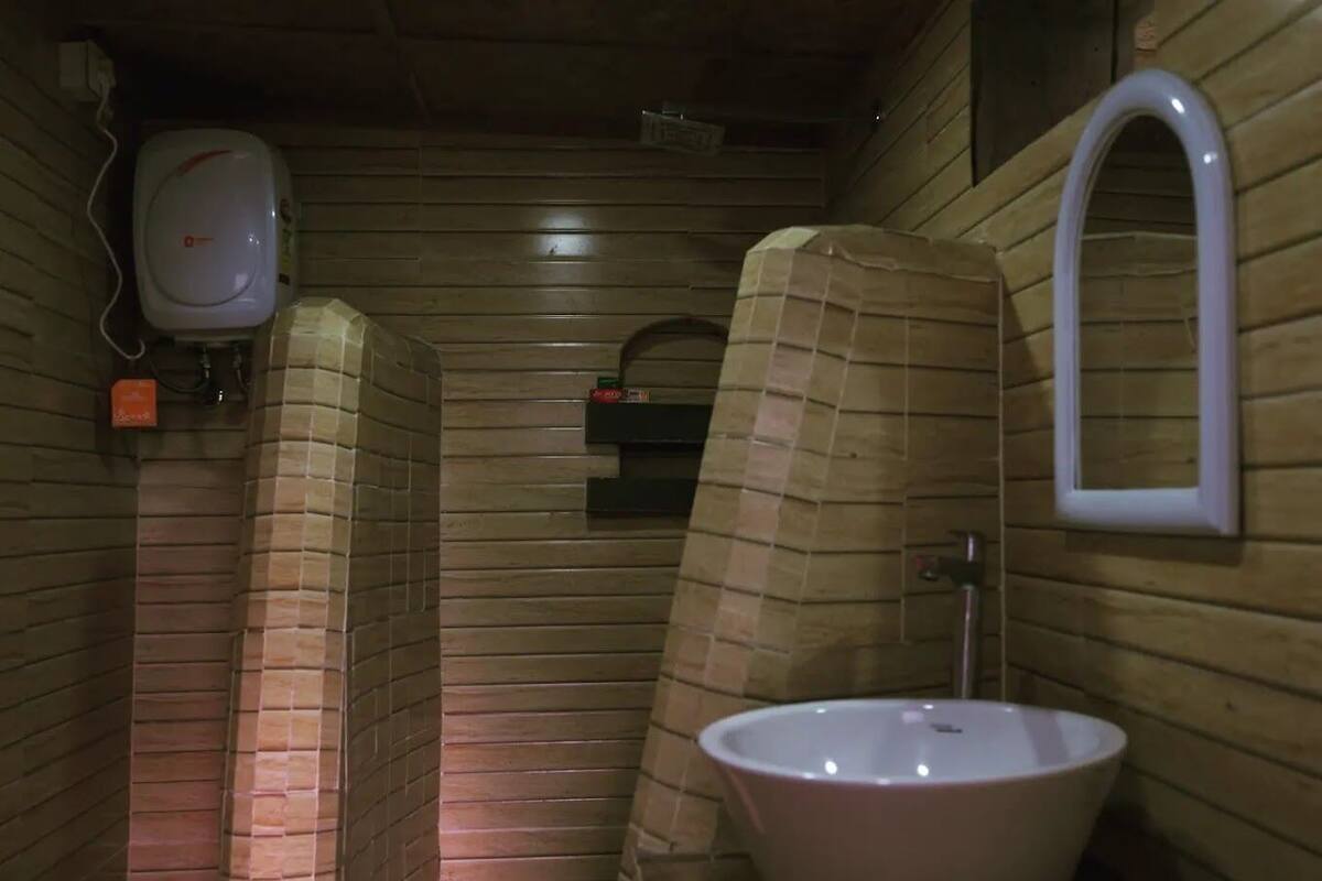 A small, enclosed bathroom with a white sink, a mirror, and a soap dispenser.