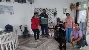 Quarto com quadro branco, uma pequena mesa com copos, uma cadeira e uma janela grande com vista para o verde lá fora.